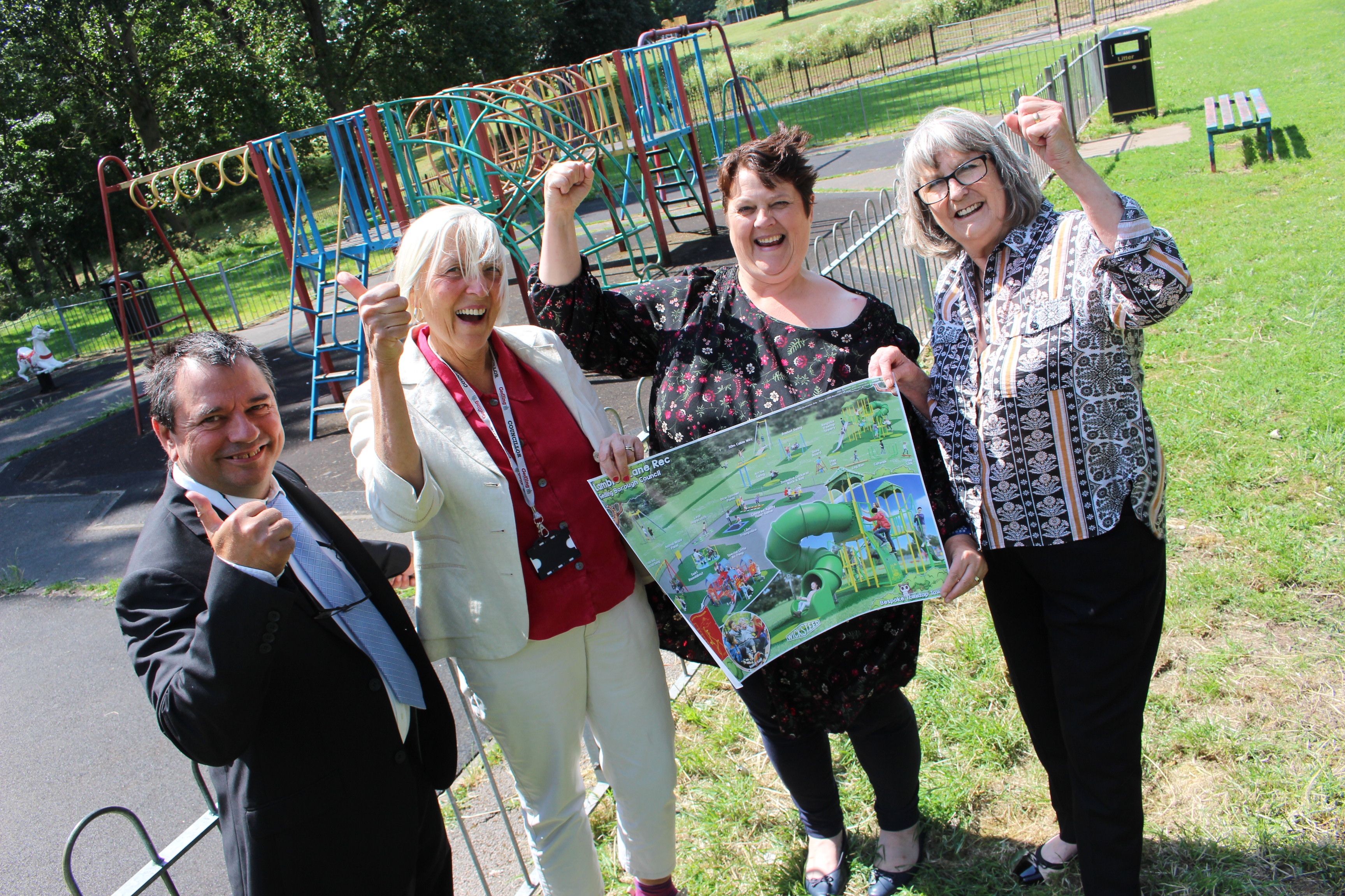 Group of people stood outside a play area at Lambley Lane. The group are holding a laminated poster with designs for a new park on it.